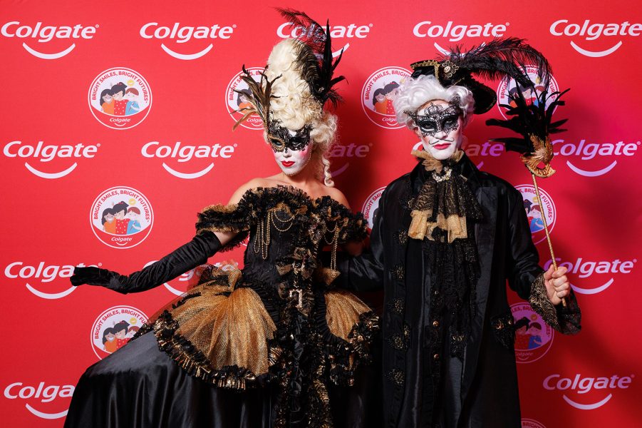 Two characters standing in front of a Colgate media wall